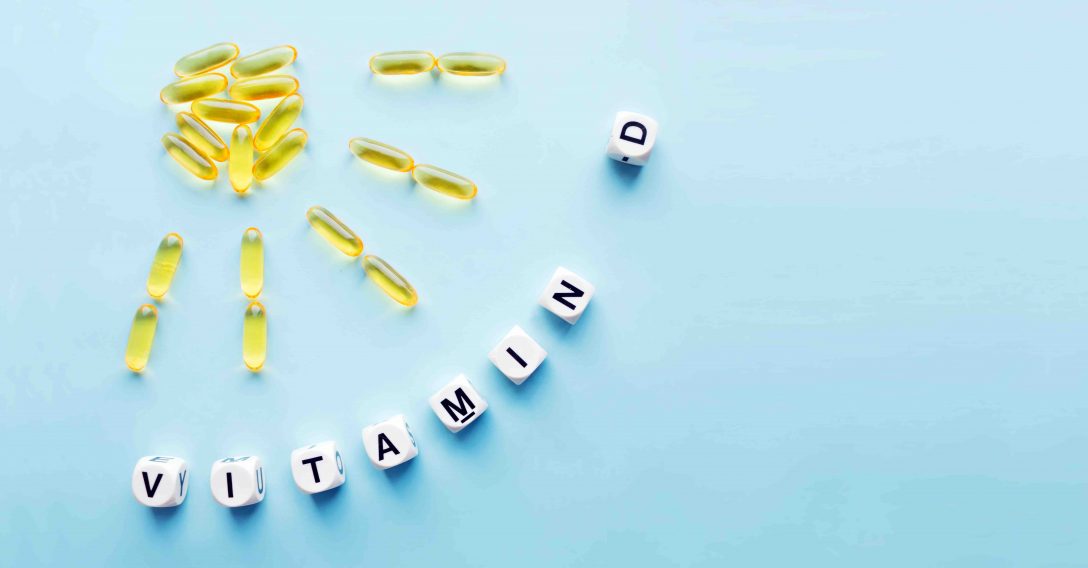 Yellow capsules in the form of the sun with rays and the word vitamin D from white cubes with letters on a blue background. VITAMIN D word for healthy and medical concept. Sunshine vitamin health benefits