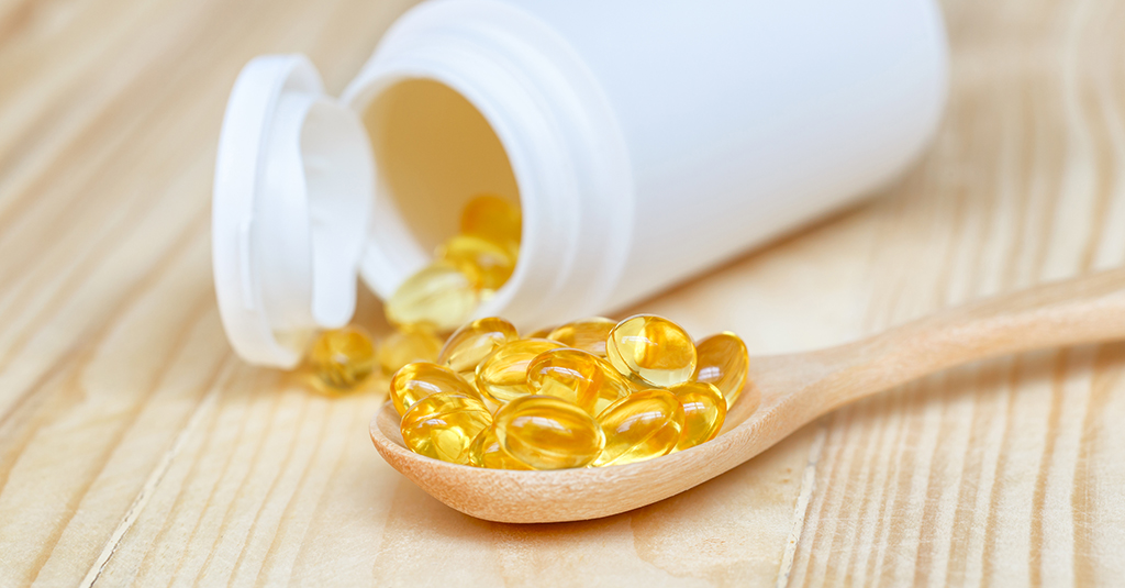 Fish oil capsules with omega 3 and vitamin D on spoon wood with in a bottle on wooden texture, healthy diet concept