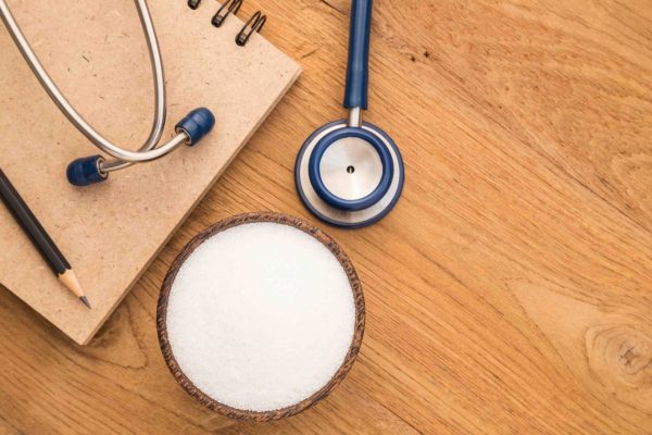 Top view blue stethoscope, sugar and note book on wooden plank background.