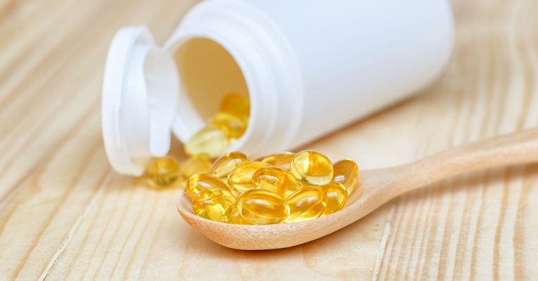 Fish oil capsules with omega 3 and vitamin D on spoon wood with in a bottle on wooden texture, healthy diet concept